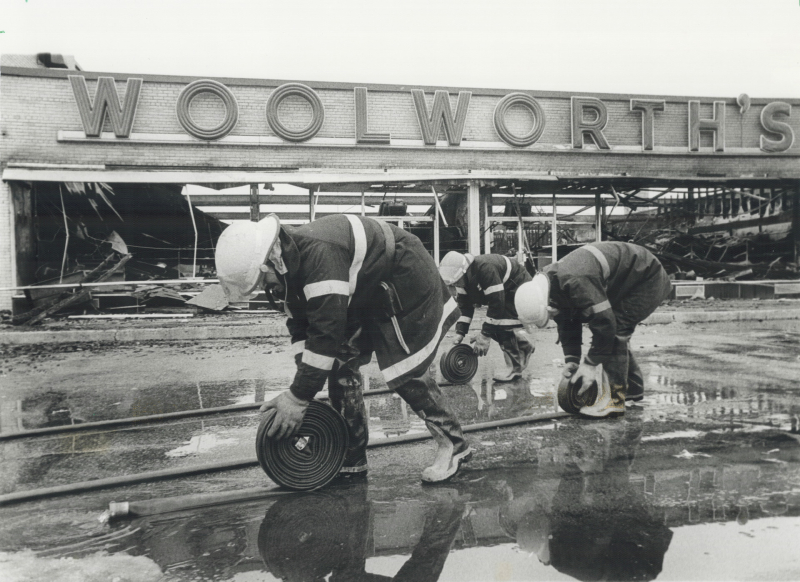 Three fire fighters rolling up hoses in front of of a burnt Woolworth's building Three fire fighters rolling up hoses in front of of a burnt Woolworth's building