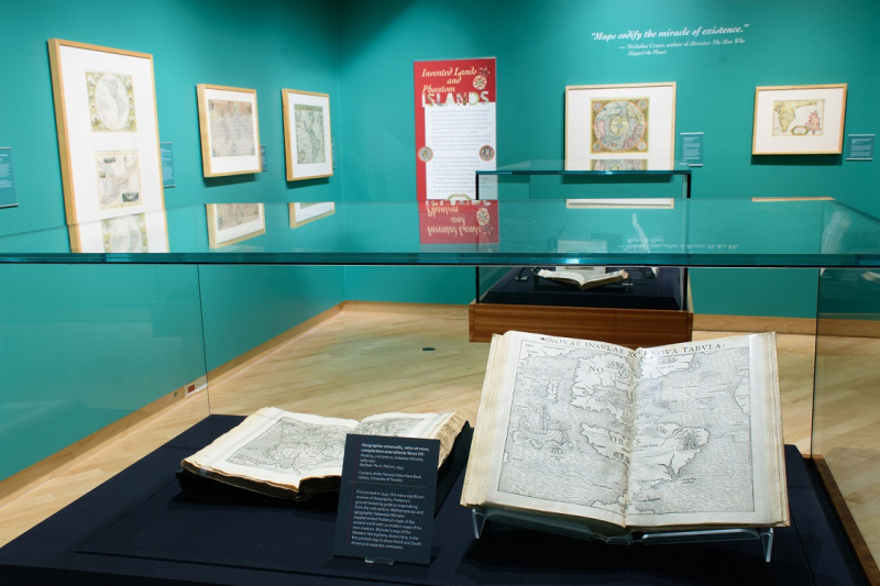 Inside a glass museum display case an atlas is shown open 