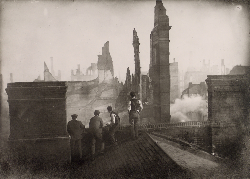 Four men on a roof looking out at ruins from a fire Four men on a roof looking out at ruins from a fire