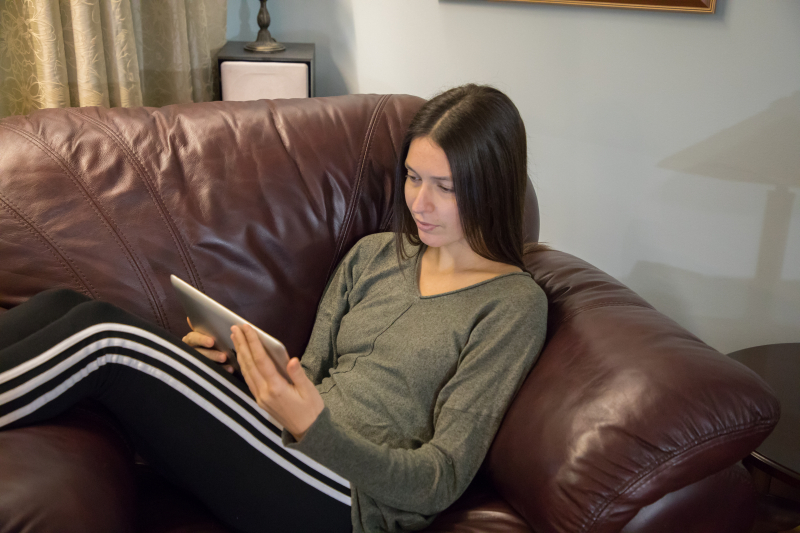 A woman sitting on a couch reading on a tablet.