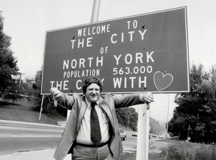 Howard Moscoe standing in front of a City of North York Boundary sign with two thumbs down 1980 Howard Moscoe standing in front of a City of North York Boundary sign with two thumbs down 1980