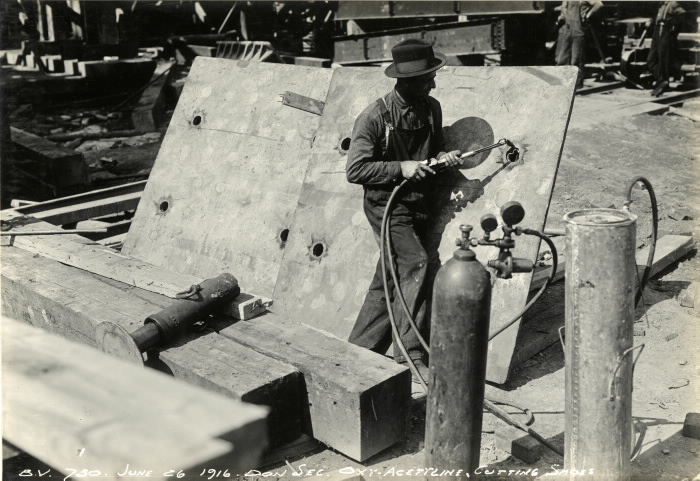 Man in overalls with tool hooke up to canister cutting holes in metal