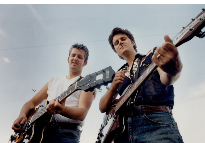 Two men with guitars posing with a blue sky behind them Two men with guitars posing with a blue sky behind them