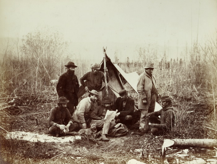 Men and dog resting at a temporary camping location with tent in the outdoors