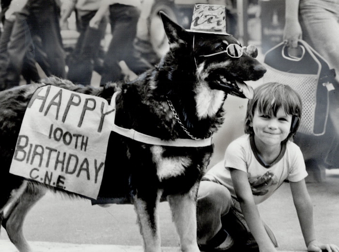 Dog with hat and sunglasses and sign that reads Happy 100th Birthday CNE