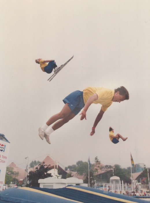 Three men in matching uniforms bouned high in the air one of which has skis