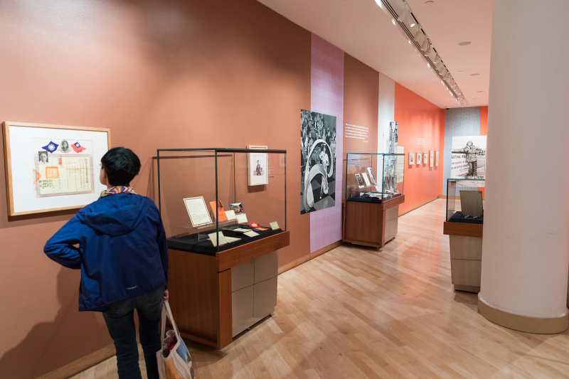 Interior of gallery with cases with items and a person examining a Chinese document displayed in a frame