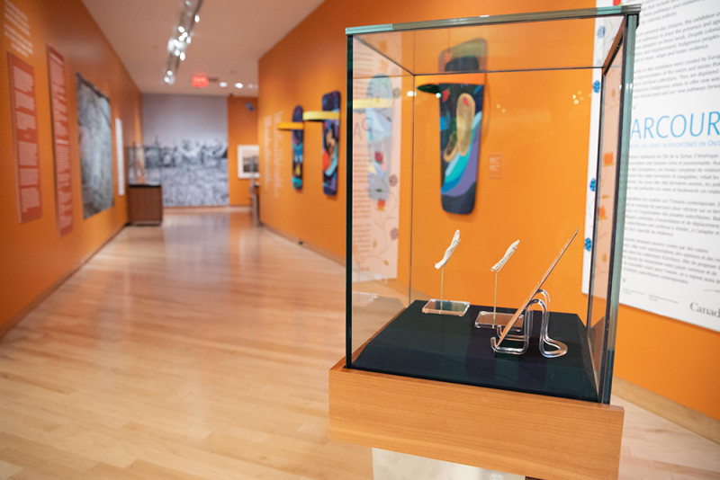 Interior of gallery with case in focus with objects inside and beyond colourful artwork