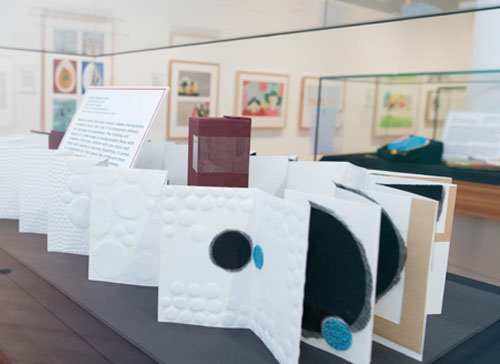 Accordion style book unfolded in a display case with pages full of white circles and other shapes