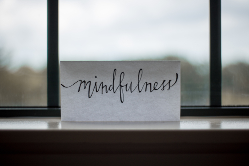A piece of paper in front of a window with the word mindfulness handwritten on it. 