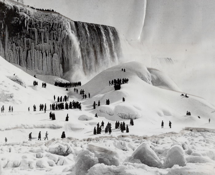 Crowds gather on a snowy landscape with waterfall in background
