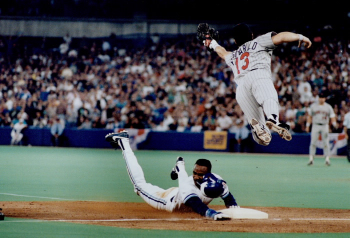 Baseball player slides into plate as another player jumps mid air