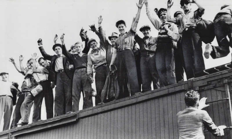 Vintage photo of many men in working clothes waving on top of train