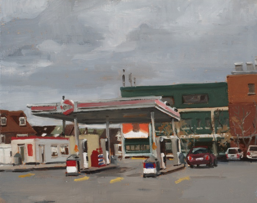An empty gas station with red signage is in the foreground and a large green industrial building appears in background.