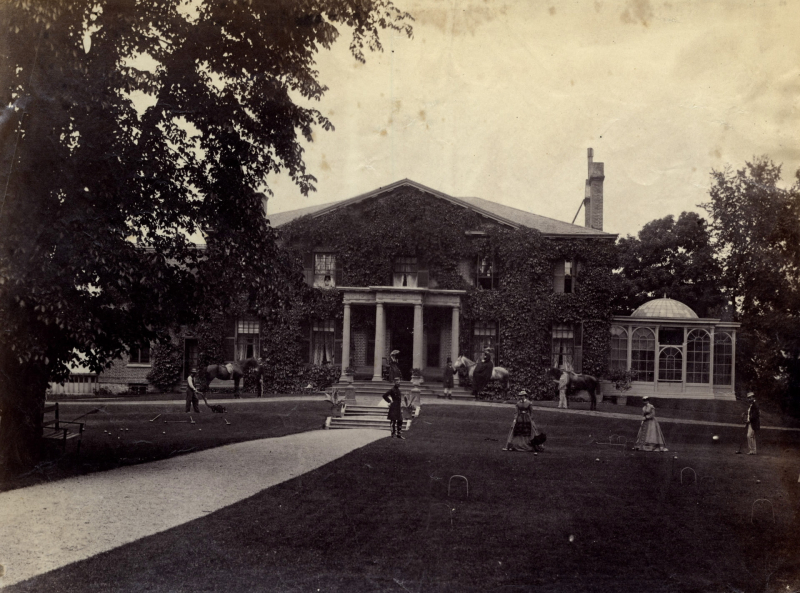 Large ivy covered mansion with men and women playing lawn sports on front yard