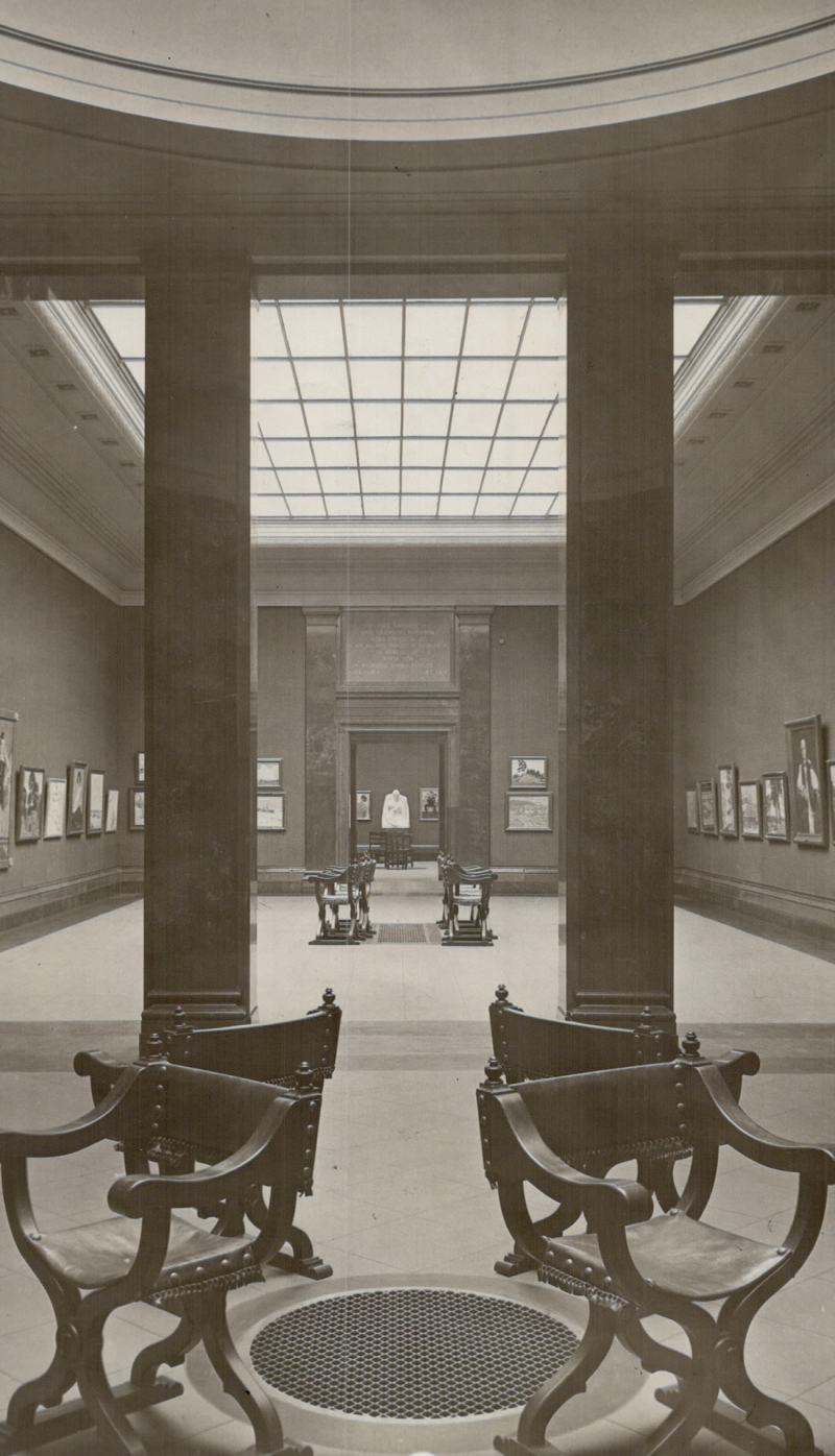 Vintage photograph of large interior exhibit space with paintings on wall and chairs in middle of room