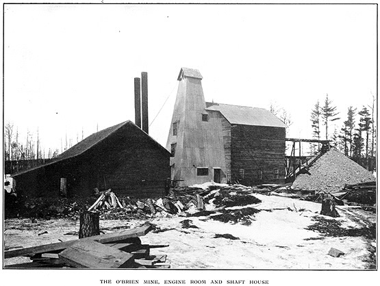 View of two wood buildings with lumber nearby and subtitle The O'Brien Mine Engine Room and Shaft House
