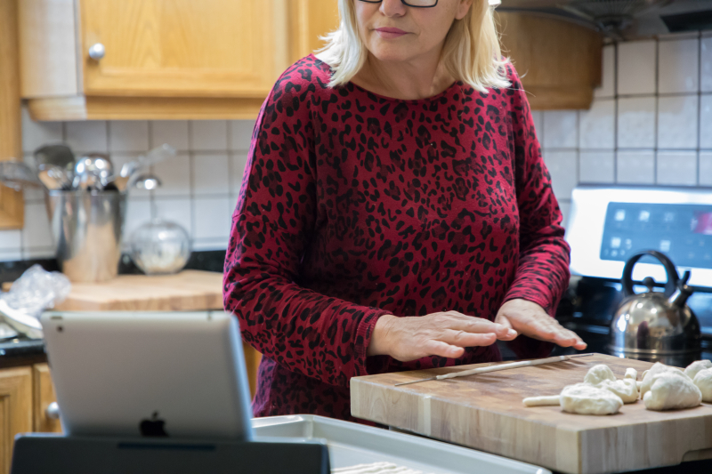 Woman rolling out dough while looking at a tablet