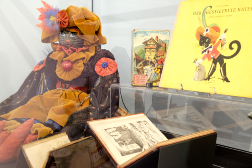Glass display case featuring versions of Puss in Boots including a marrionette