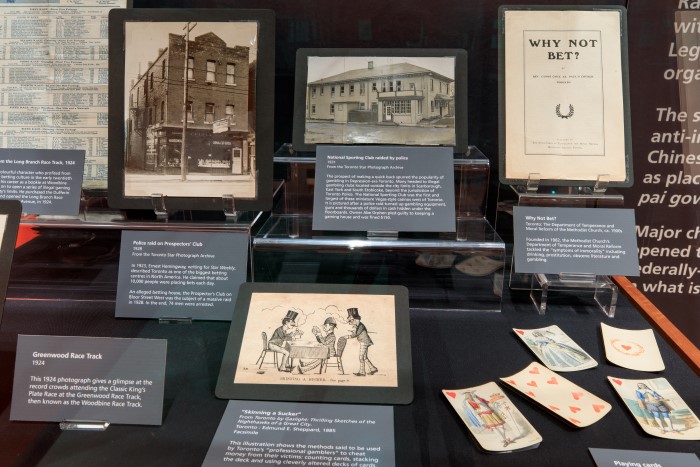 A display case with photographs and ephemera related to gambling in Toronto. Playing cards are displayed at right. 