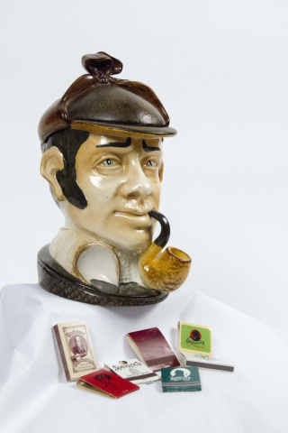 A ceramic humidor appears as a bust of Sherlock Holmes. Several matchbooks are displayed below. 