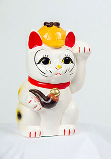 A white ceramic Maneki-neko cat wears a deerstalker hat and holds a pipe
