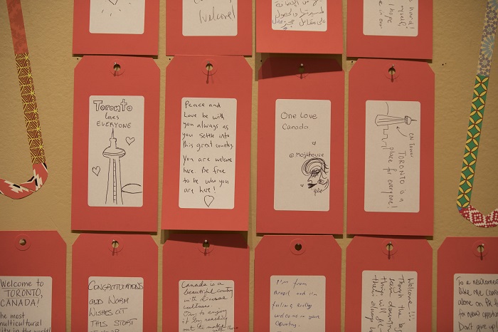 A close up image of handwritten tags left by visitors for recent newcomers. Messages include "Toronto love everyone" and "Peace and love be with you always as you settle into this great country. You are welcome here. Be free to be who you are here!"