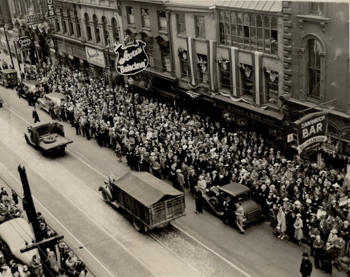 Vintage image of packed sidewalks in urban area with a few military style vehicles on the empty road