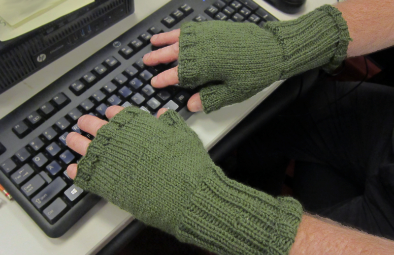 Hands at keyboard with knitted gloved with top half of fingers and thumb exposed