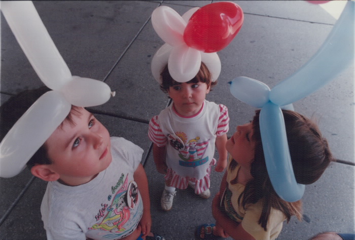 Three children wearing hats made out of balloons.