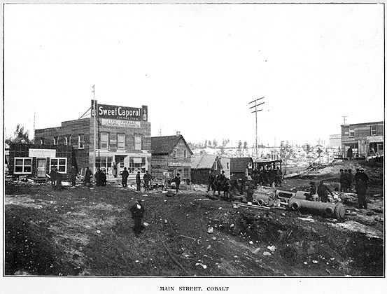 Cluster of vintage buildings amidst gravelly path with a few men visible