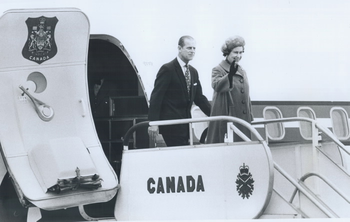 Queen and husband disembarking plane with Canada written on side of steps and Queen waving