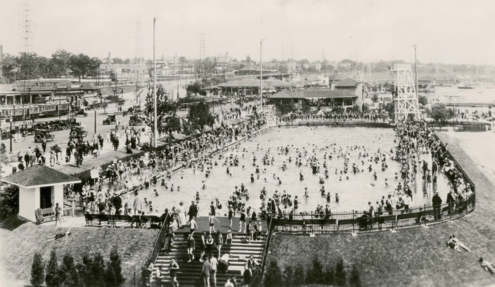 Large outdoor pool with lots of swimmers and people on the sides of it Large outdoor pool with lots of swimmers and people on the sides of it