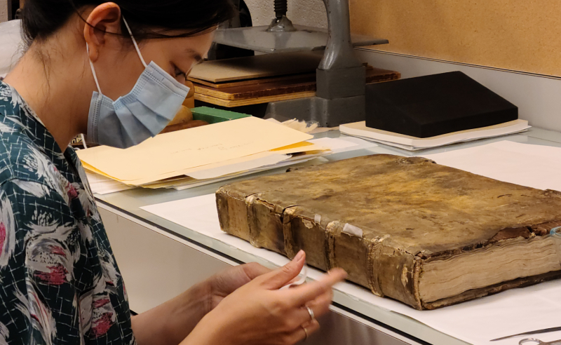 Conservator in mask handling old book in lab
