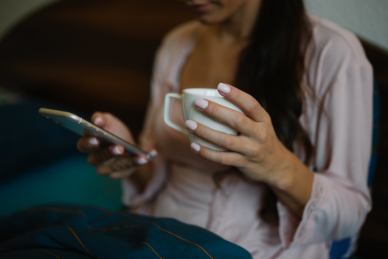 Woman looking at phone in one hand, and holding a cup in the other