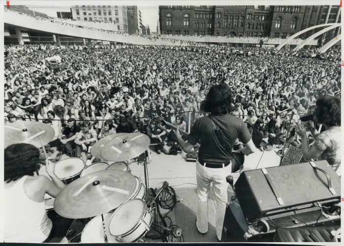 View of large crowd from behind a band on stage