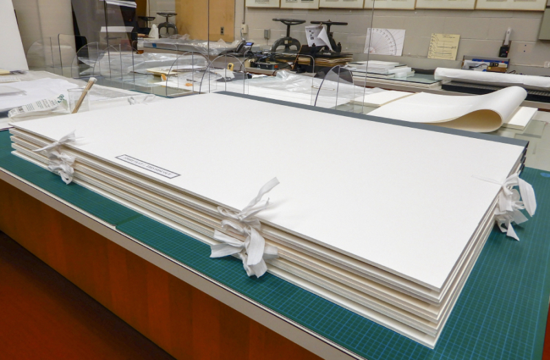 Four portfolios are stacked on a work bench in a conservation lab