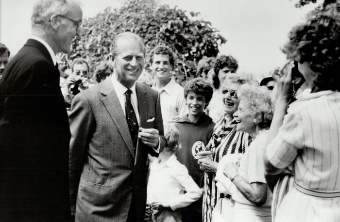 Prince Philip smiling with crowd of different ages surrounding him and a photographer taking his picture Prince Philip smiling with crowd of different ages surrounding him and a photographer taking his picture