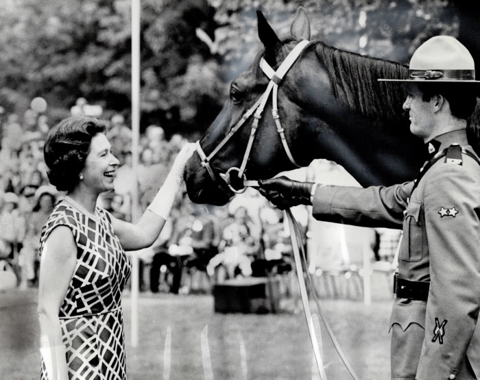 Queen patting horse beside Canadian mountie