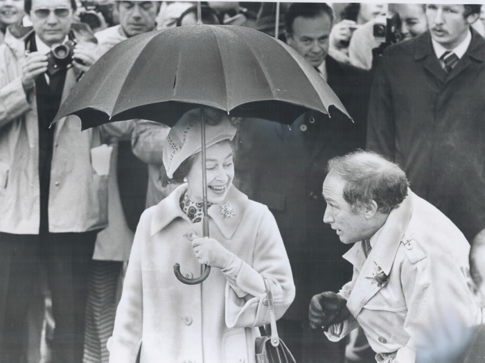 Queen holding umbrella as Pierre Trudeau crouches underneat umbreela