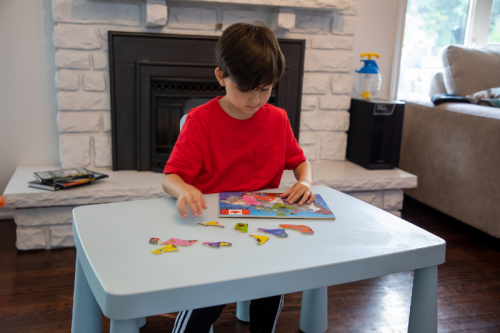 Kid sitting at a table and working on a jigsaw puzzle. There is a fireplace and partially seen sofa in the background. Kid sitting at a table and working on a jigsaw puzzle. There is a fireplace and partially seen sofa in the background.
