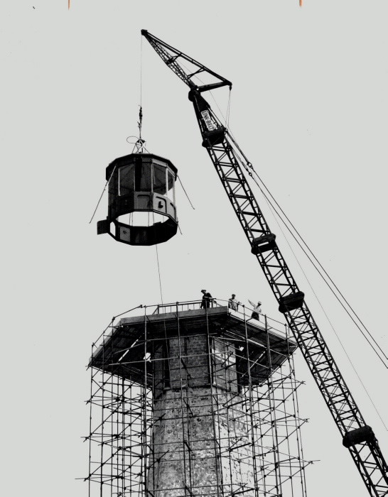 Top of lighthouse held by crane above scaffolding around lighthouse with workers Top of lighthouse held by crane above scaffolding around lighthouse with workers