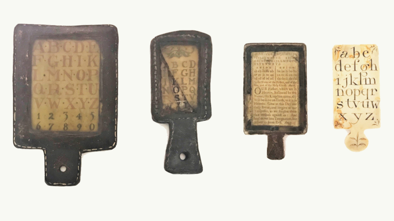 Four hornbook specimens, three of the hornbooks are made of leather and one hornbook is made of ivory and letters of alphabet visible