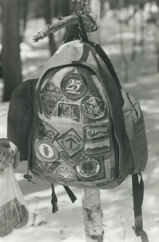 Close-up photo of a backpack covered in patches, hung on a stick.