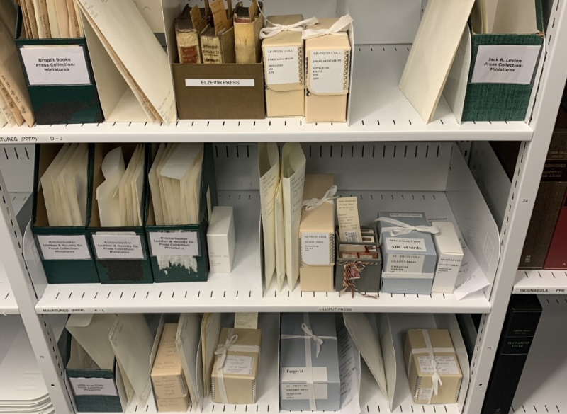 Shelves of archival materials labelled including a section on one shelf for miniature books