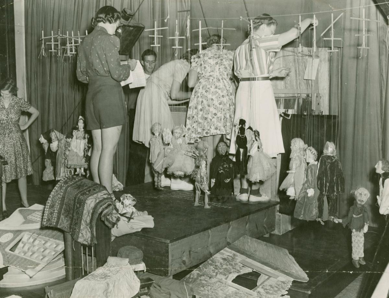 Picture of a group of people standing on a stage setting up puppets for a puppet show