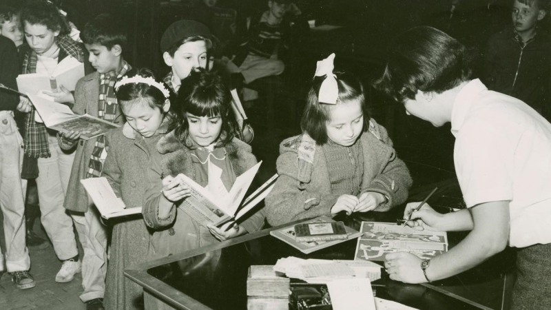 Line of children holding books wait to check out their library books