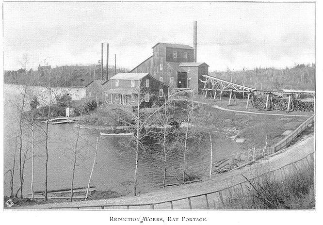 Framed black and white vintage photo of dirt road leading to a industrial building by water