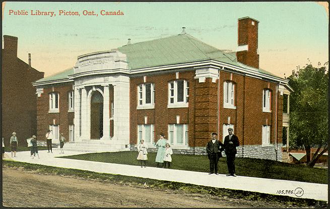 Red brick library building with people standing on the sidewalk out front. 