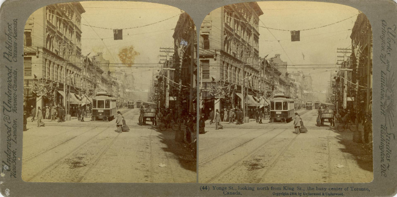 Two side by side images of what appears to be the same image of an old street with as streetcar and many people on sidewalks as well as some flags and crowns hanging on stores and above street